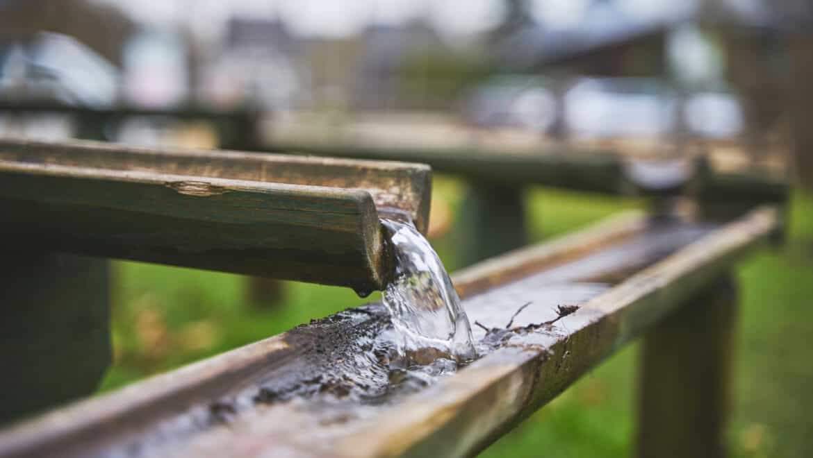 Wasser fließt durch eine Holzrinne, Symbol für Wasser im Handwerk.