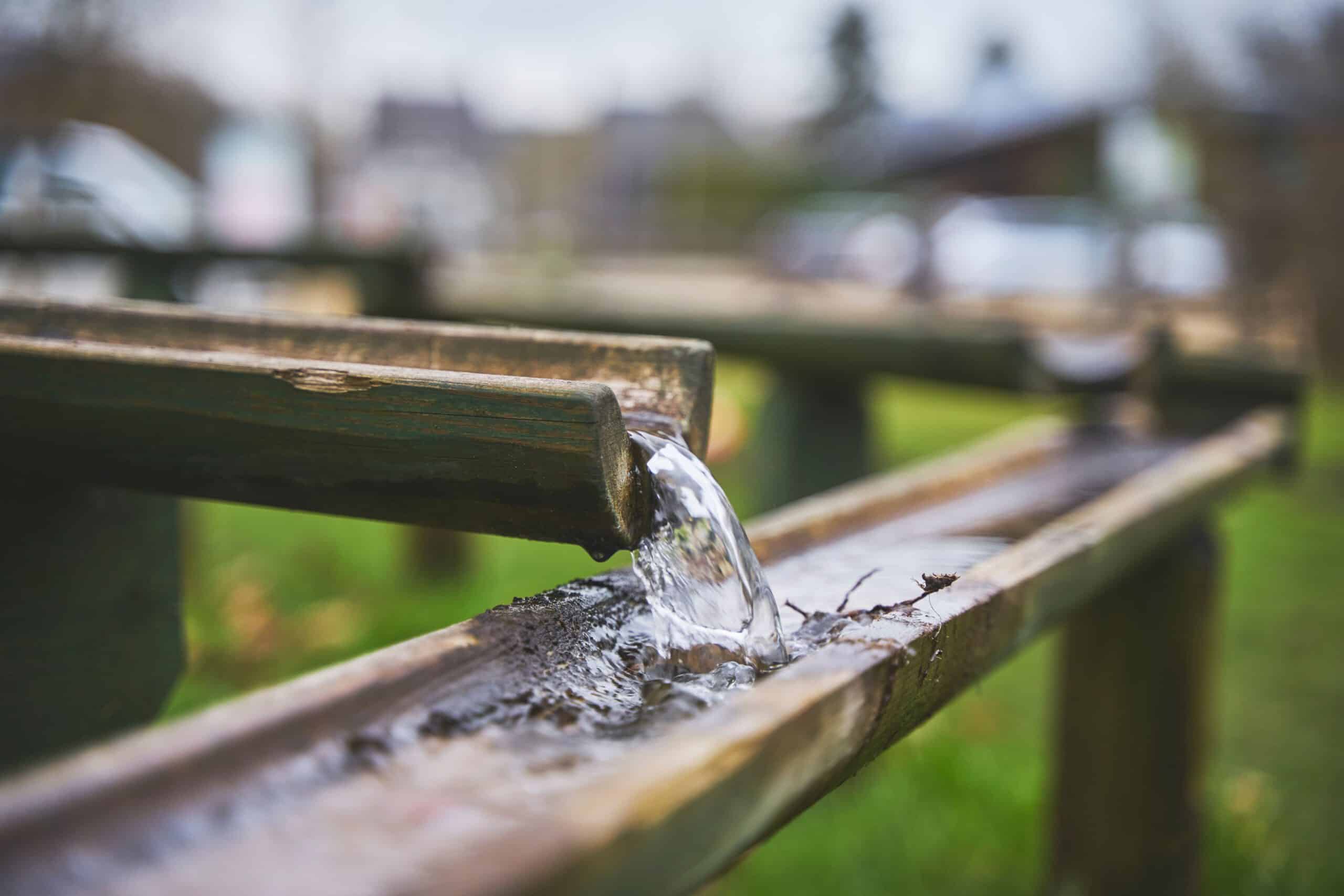 Wasser fließt durch eine Holzrinne, Symbol für Wasser im Handwerk.